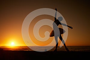 Silhouette of a ballet dancer at dancing on the beach at sunset. Graceful slender ballerina dancing outdoors