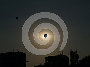 A silhouette of a balloon in the middle of sun with silhouettes of suburb, Balloon Day Hradec Kralove