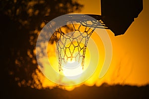 Silhouette of a basketball hoop against a golden sky during the sunset