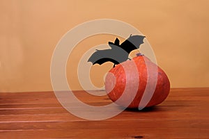 Silhouette of a bat near a pumpkin on wooden table against yellow background. Halloween concept photo