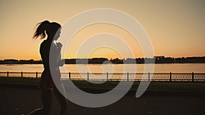 Silhouette of a beautiful asian girl run along the river. Taste of freedom. Playing sports at sunrise or sunset. Solo