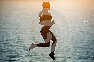 Silhouette of a beautiful, athletic woman jumping during sports near the river at sunset.