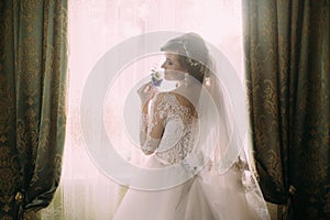 Silhouette of beautiful bride in traditional white wedding dress, stood by window.