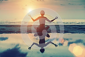 Silhouette of beautiful girl sitting on the beach and meditating in yoga pose.