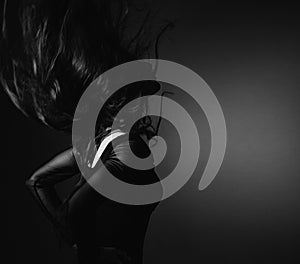 Silhouette of beautiful girl with sporty slim figure in black dress moving with hair above the head on dark shadow art background