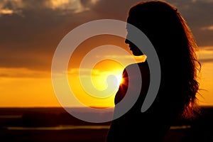 Silhouette of a beautiful girl at sunset, face profile of young woman enjoying nature
