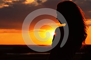 Silhouette of a beautiful girl at sunset in a field, face profile of young woman enjoying nature