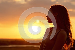 Silhouette of a beautiful girl at sunset in a field, face profile of young woman enjoying nature