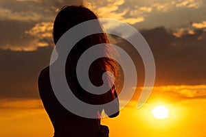 Silhouette of a beautiful romantic girl at sunset , face profile of young woman with long hair in hot weather