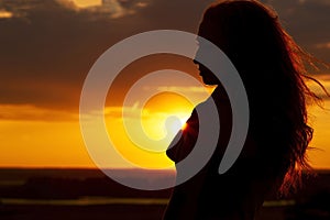 Silhouette of a beautiful romantic girl at sunset , face profile of young woman with long hair in hot weather