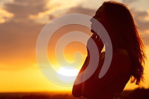 Silhouette of a beautiful romantic girl at sunset , face profile of young woman with long hair in hot weather