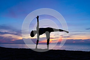 Silhouette of beautiful woman practicing yoga asana on the beach with sunrise on twilight blue vibrant sky