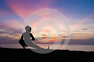 Silhouette of beautiful woman practicing yoga asana on the beach with sunrise on twilight blue vibrant sky