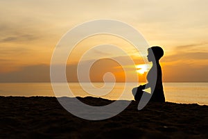 Silhouette of beautiful woman sitting cross legged in easy seat pose on the beach with sunrise in background