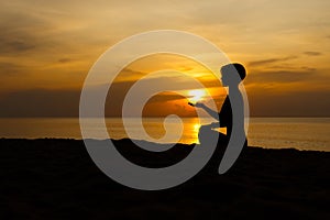 Silhouette of beautiful woman sitting cross legged in easy seat pose on the beach with sunrise in background