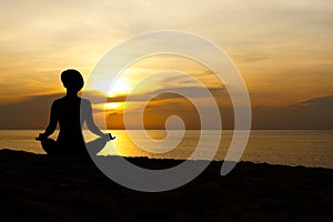 Silhouette of beautiful woman sitting cross legged in easy seat pose on the beach with sunrise in background