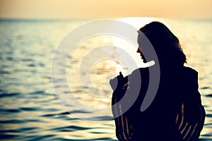 Silhouette of a beautiful woman standing with her back to the camera in the sea water at sunrise holding a large wide-brimmed hat