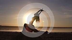 Silhouette of beautiful yoga woman in the morning sky on a sea beach. A woman practicing yoga Virabhadrasana II Warrior