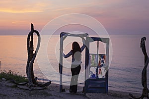 Silhouette of a beautiful young red haired girl on a blue door with colorful glass waching the sunrise over the sea