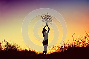 Silhouette of beautiful young woman holding a bouquet over her head at sunset prairie