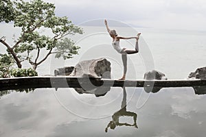 Silhouette of a beautiful young woman practicing yoga in front of the lake at sunrise.