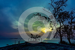 Silhouette of bicycle on the beach against colorful sunrise in t