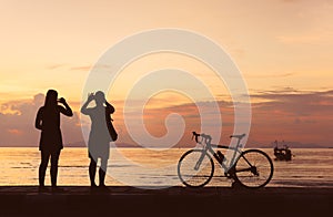 Silhouette bicycle and people take photo at beach sunset backgro