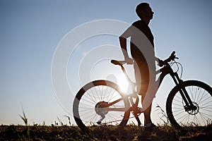 The silhouette of a bicycle and rider against the blue sky at sunset