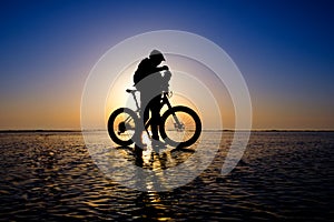 Silhouette of bicyclist standing on the clear ice