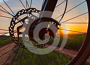 Silhouette of a bike wheel with disc brake and spokes and setting sun in the background