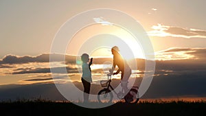 Silhouette biker lovely family on the meadow at sunset time. Silhouette of mother and baby biking at sunset. Lifestyle
