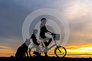 Silhouette biker lovely family at sunset over the ocean. Mom and daughter with dog bicycling at the beach.