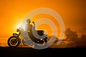 Silhouette of biker man sitting smokes with his motorbike beside the natural lake and beautiful, enjoying freedom and active lifes