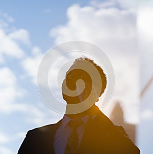 silhouette of black businessman with blue suit and tie using mobile, calling, working outside building in city with sunrise