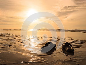 Silhouette black sandals on sand at golden sunset beach