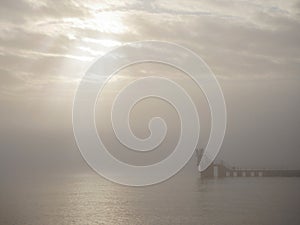Silhouette of Blackrock public diving tower in a fog. Cloudy sky over ocean with sun beams bursting through clouds. Calm and