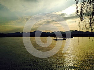 A silhouette boat and man sailing on the calm sea at sunset in the background of mountains and sun beams.