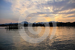 A silhouette boat and man sailing on the calm sea at sunset in the background of mountains and sun beams.