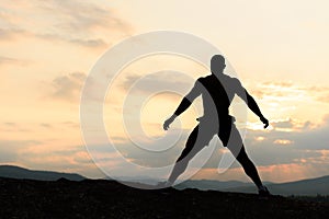 Silhouette of bodybuilder posing at the sunrise or sunset in mountains. Handsome strong man showing his muscles