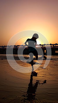 Silhouette of a boy at the beach against a bridge during sunset