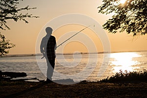 Silhouette of a boy fishing on a lake in the summer at sunset