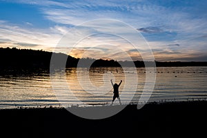 Silhouette of boy with hands in the air on the beach in twilight