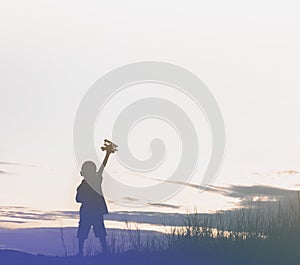 Silhouette boy playing with toy airplane sunset