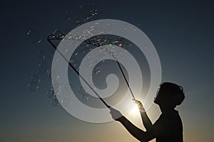 Silhouette boy playing witah a bubble wand