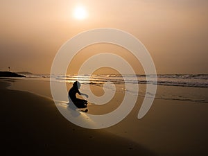 Silhouette of a boy seating on the shoreline of a caribbean beach near Cartagena Colombia during sunset