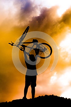 Silhouette of a boy standing up a mountain bike at sunset