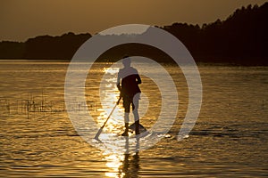 Silhouette boy on sup-board stand up paddle board in late evening during sunset