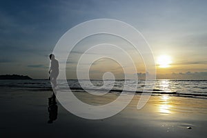 Silhouette of a Boy Walking on the beach at sunset backdrop.