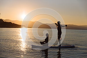 Silhouette of boy in yoga pose and girl sitting on sup surf at the ocean. Concept lifestyle, sport, love