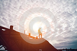 Silhouette of brave man standing on the top of constructions at sunset